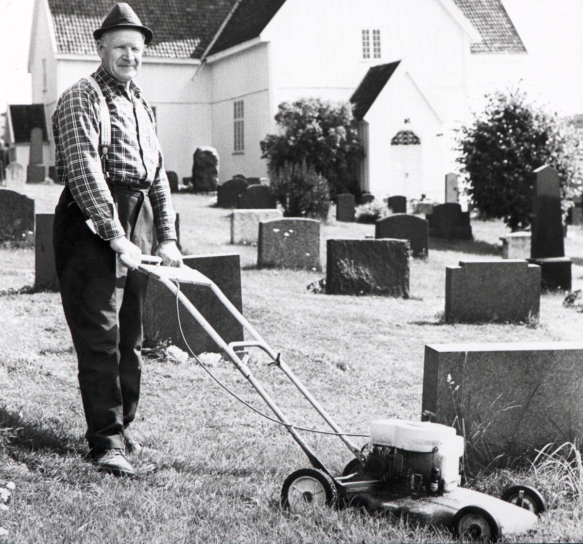 Ukjent, Veldre kirke, Kirketjener Gunnar Solli i over 40 år, klipper plenen på kirkegården, 1975.
