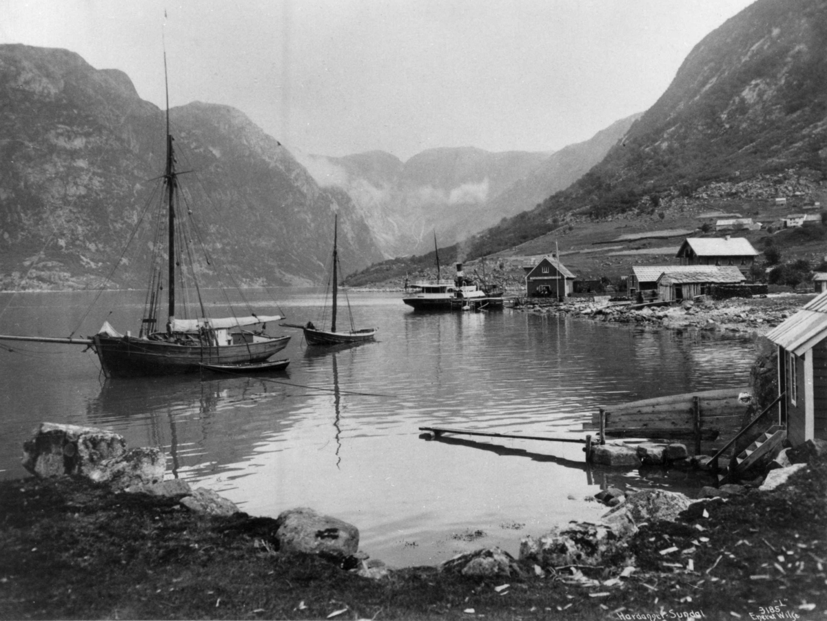 Axel Lindahl, Seilbåt og dampskip på fjorden i Sundal i Mauranger i Kvinnherad i Hordaland. Naust, brygge og fjell. Fotografert i perioden 1885 - 1892.
