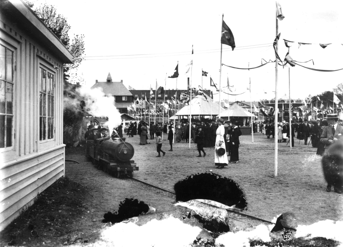 Hermann Christian Neupert, Jubileumsutstillingen på Frogner, Oslo, 1914. Lilleputtbane. Publikum og paviljonger i bakgrunnen. Flagg.