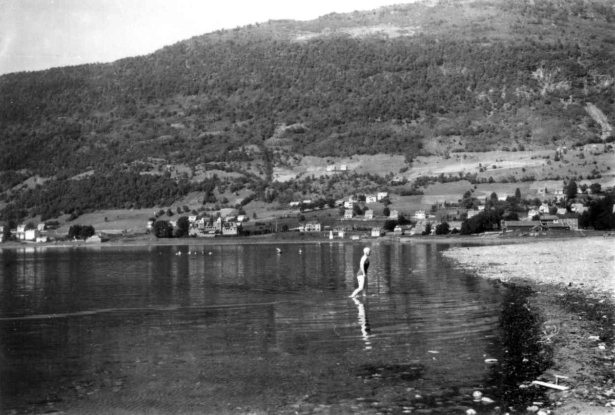 Hermann Christian Neupert, Voss 1939. Vangsvatnet. Bebyggelse. En badende kvinne på vei mot stranden. Skog og fjell i bakgrunnen.
