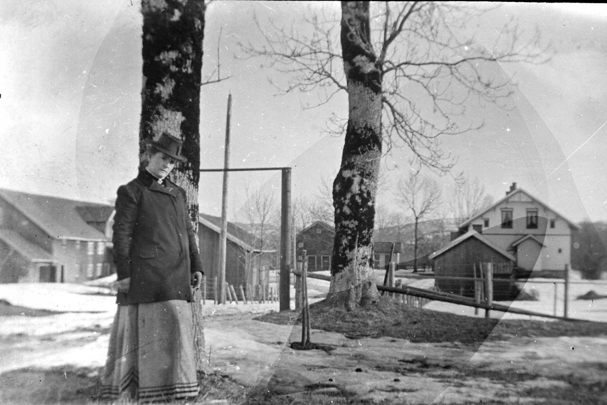 Juliane Fredrikke Langberg, Portrett av kvinne foran Hurum prestegård vinterstid. Hun er kledd i fotsidt skjørt/kjole, ytterjakke og hatt. Fra malerinne Juliane Fredrikke Langbergs (1856-1930) samling, tatt ca.1895-1910 med motivkrets slekt og venner samt steder tilknyttet samvær med disse.