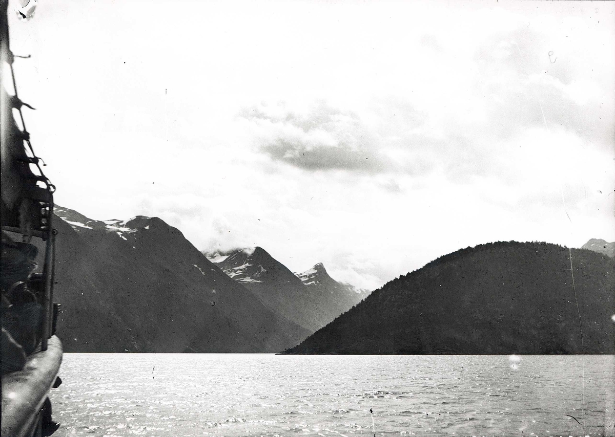 Tom Kent, Fjordlandskap med skog og snøtoppede fjell. Skipsreling synlig på venstre side.
