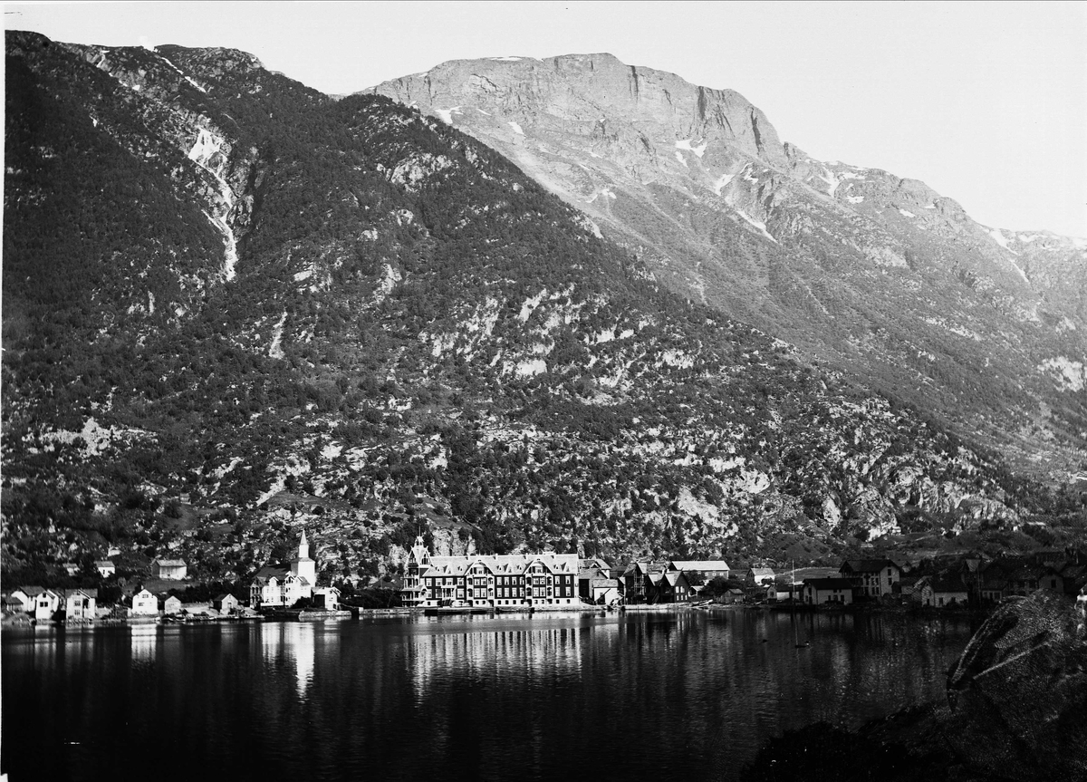 Solveig Lund, Landskapsfotografi fra Odda i Hardanger. I forgrunnen sees Sørfjorden og i bakgrunnen fjell. I midten sees Odda med kirken og Hardanger hotell.