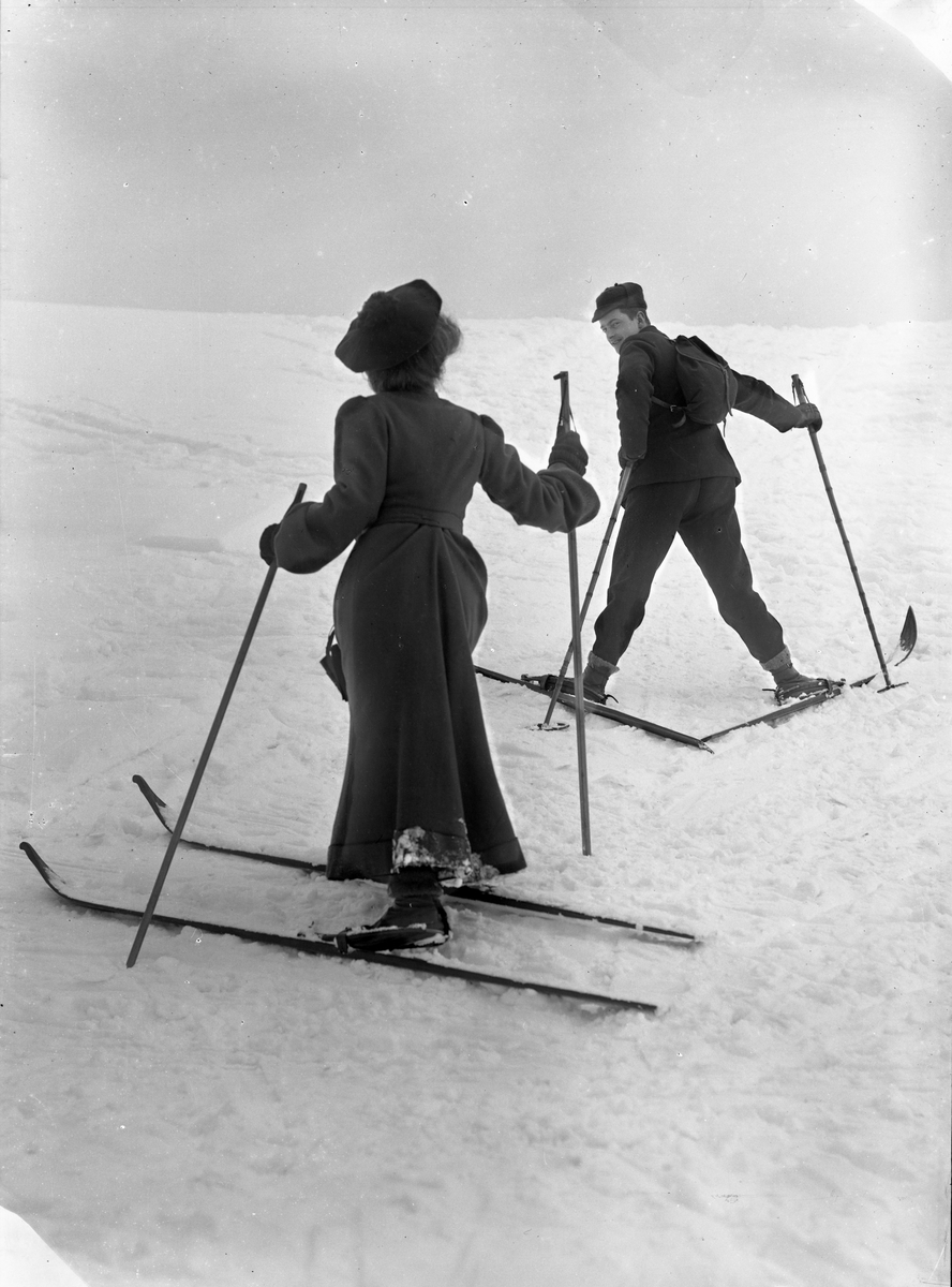 Solveig Lund, Mann og kvinne i snødekt landskap. Fotografert bakfra gående oppover en bakke - begge med ski på beina.