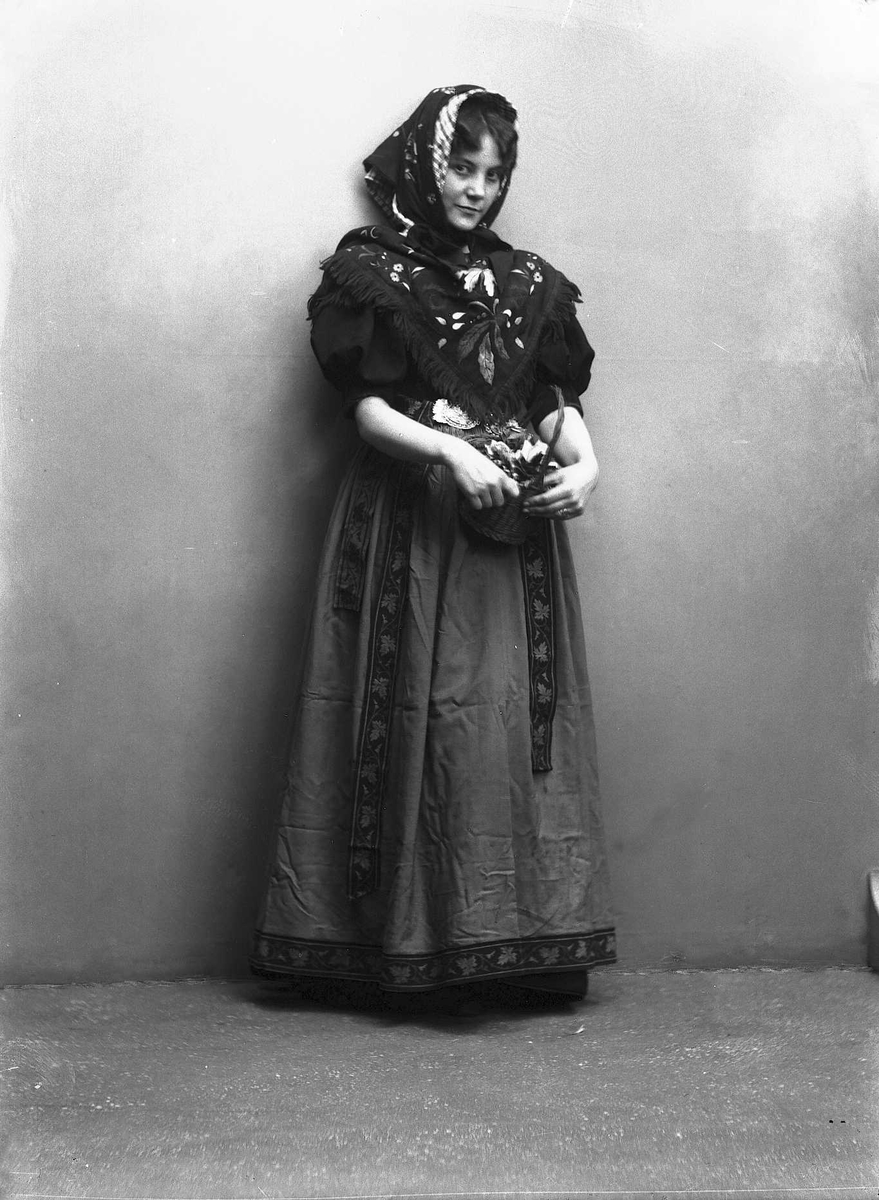 Solveig Lund, Studioportrett av kvinne i drakt og skaut, som holder en kurv med roser i armene. Avfotografert foran en nøytral bakgrunn.