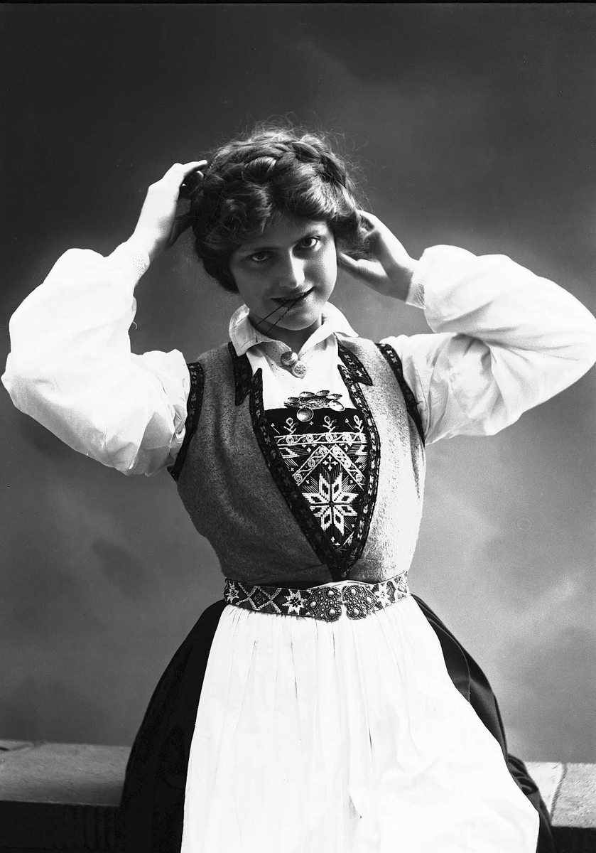 Solveig Lund, Studioportrett av kvinne i drakt som setter opp håret. Hun har spenne i munnen.
