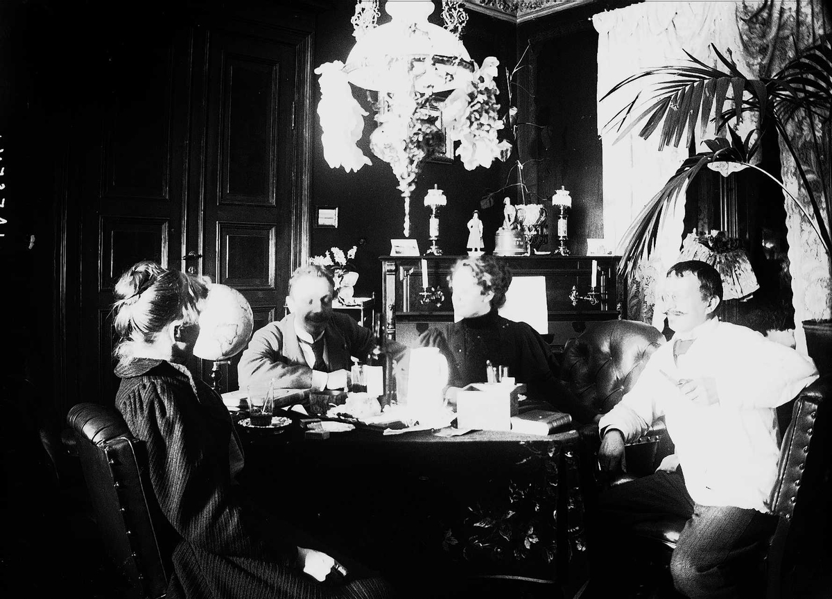 Axel Quinsgaard Wiborg, Stueinteriør, Munkedamsveien 65B, Oslo. 1903, med mennesker rundt bord, Gudrun Q, Wiborg, Edle Thoresen, hr. Møller, Axel Q. Wiborg.