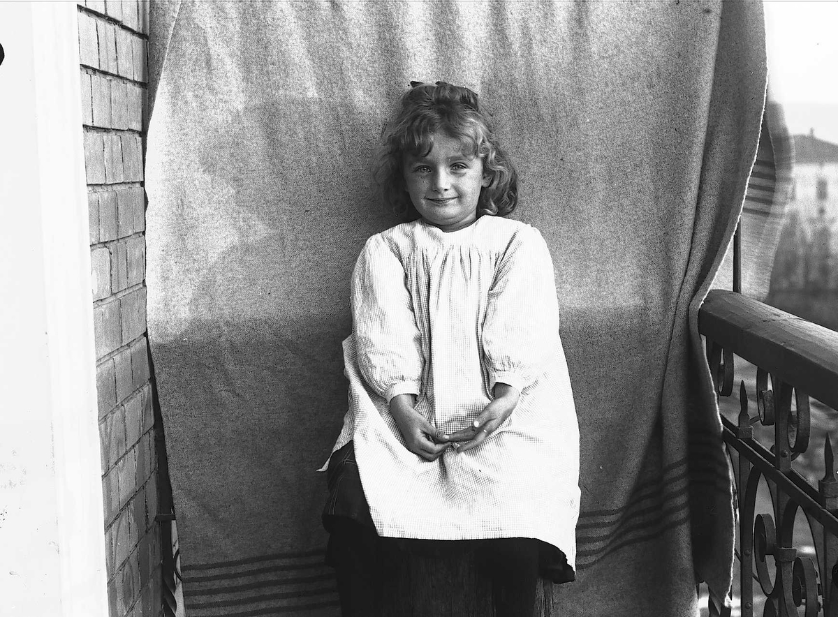 Axel Quinsgaard Wiborg, Karen Q. Wiborg fotografert på balkong, ant. Meltzers gate 9, Oslo, 1899, mot opphengt bakteppe.