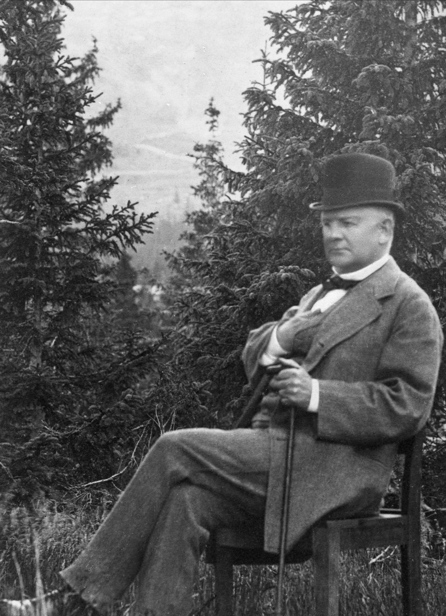 Gustav Borgen, Avfotografering. Mann på stol med granskog i bakgrunnen.