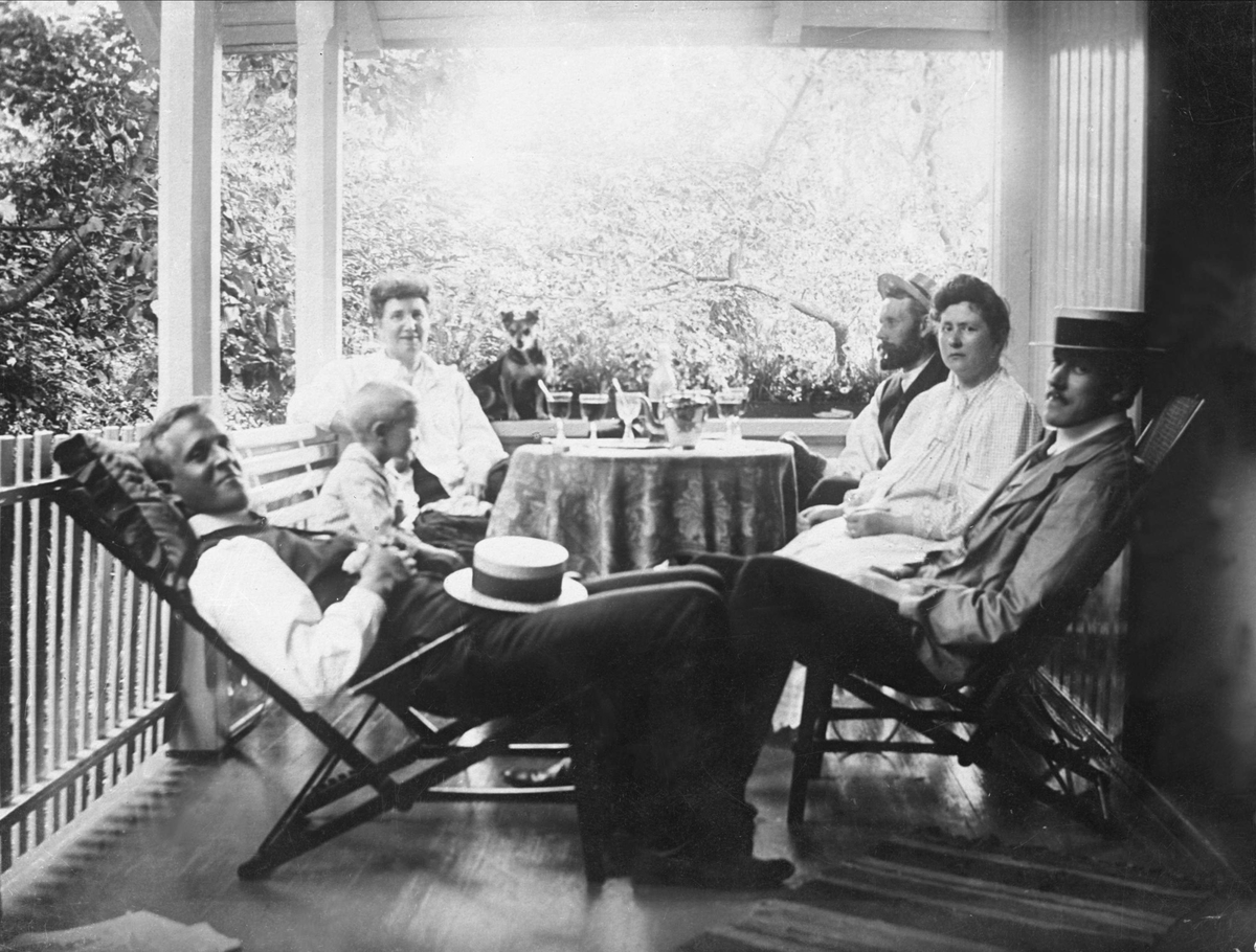 Gustav Borgen, Avfotografering. Familie sittende ute på verandaen. Tre menn, to kvinner, en gutt og en liten hund.