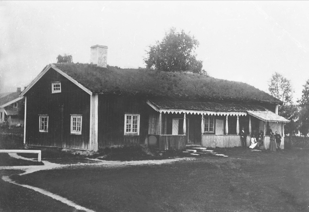Gustav Borgen, Avfotografering. Lang og smal tømmerstue, panelt, med torvtak. Folk foran på høyre side.