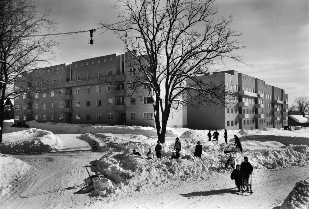 Anno Domkirkeodden, EKSTERIØR CHRISTIEBYGGET, FRA KRYSSET ST. OLAVSGATE/PARKGATA, BARN LEKER I SNØEN, VINTER. Sparkstøtting. Brøytekanter. Gatebelysning.