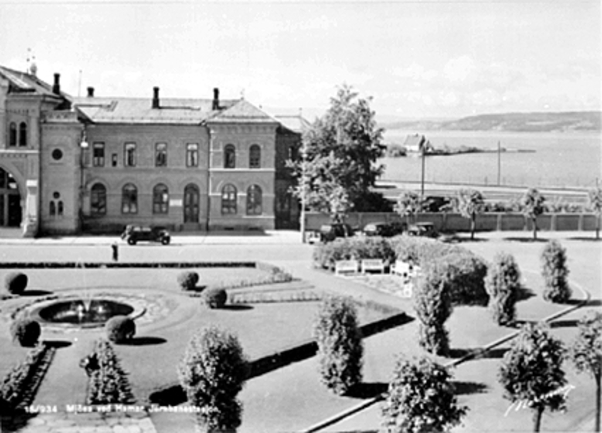 Anno Domkirkeodden, FRA JERNBANEPLASSEN MED STASJONSBYGNINGEN TIL VENSTRE MOT PUMPEHUSET PÅ TJUVHOLMEN OG MJØSA I BAKGRUNNEN. Postkort.