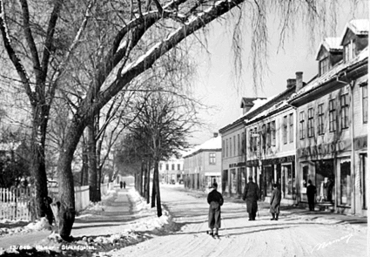 Anno Domkirkeodden, Strandgata, Strandgateparken, Hamar. Vinter, skiløper. Forretningene til Erling Vold, NEBB, Joh. H. Borgersen, Ole Jølstad, Postkort "Hamar Strandgaten"