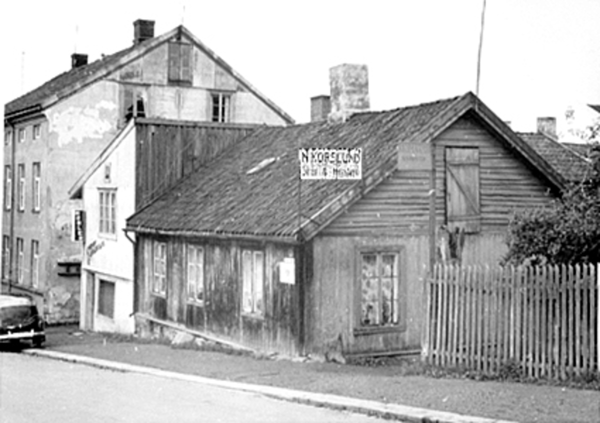 Anno Domkirkeodden, EKSTERIØR GRØNNEGATA 92, LIERBAKKEN, N. KORSLUND SMED, TEKST PÅ DE TO SKILTENE VED INNGANGEN: "N. KORSLUND SMED OG HOVSLAGER" OG "SKOMAKERVERKSTED". NEDERSTE HUSET TIL "HANSEN & DYSTVIK, SÅ KOMMER "MØBELTAPETSERER JOHANSEN". HUSENE LÅ MELLEM TORGGATA OG GRØNNEGATA. KORSLUNDGÅRDEN.