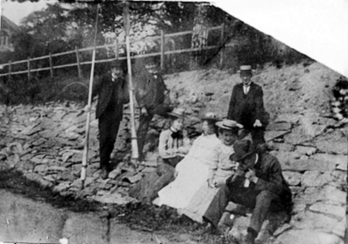 Anno Domkirkeodden, GRUPPE 7 MENN OG DAMER PÅ STEINSKRÅNING VED MJØSSTRANDA, ETTER EN ROTUR, 2 MENN MED ÅRER