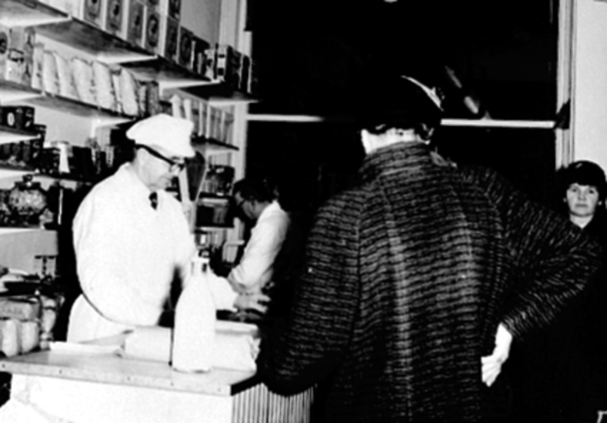 Anno Domkirkeodden, L. Nilsens Eftf. Johs. og Pernille Saugestad, Torggata 102, Hamar. Butikkinteriør, kjøpmann, kunder, melkeflaske, varehylle.