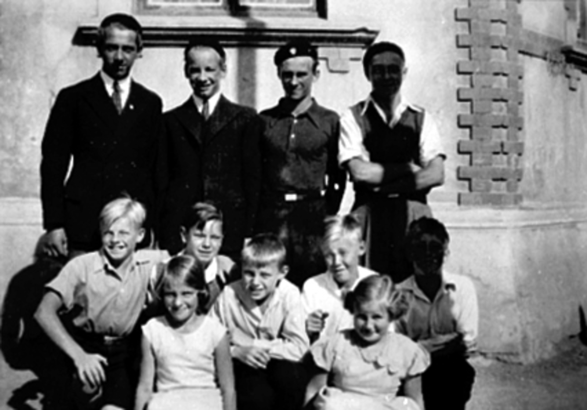 Anno Domkirkeodden, Gruppe 11, barn, voksne, ved hjørnet Grønnegata 61, Hamar. Første rekke f.v. Odvar Rye-Johnsen, Vesla Arnesen, Odd Engh, Leif Johansen, Else Stensrud, ukjent. Bak f.v. Rolf Johnsen, Gunnar Arnesen, Alf Sagstuen ("Kønnfritt"), Sigurd Johnsen. Ca. 1934.
