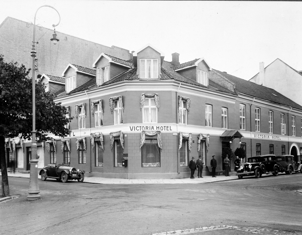 Anno Domkirkeodden, VICTORIA HOTEL, EKSTERIØR, STRANDGATA I HAMAR, ENGGATA. GRUPPE 5 FRA VENSTRE: REISENDE I TOBAKK STRØM FRA FIRMA TIEDEMANN, DIREKTØR GUNNAR KNUDSEN, HOTELLBUDET, HAGAR KNUDSEN, OG UKJENT KVINNE. D-3120 BUGATTI 1925 MODELL TILHØRTE GUNNAR KNUDSEN, HAN SOLGTE BILEN I 1931. A-9587, REO 1929 MODELL. BIL…