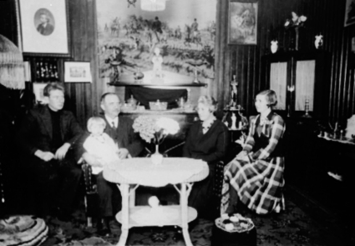 Anno Domkirkeodden, Platous gate 21, Hamar. Familiegruppe, interiør, stue. F.v. Per Nord, Karl A. Windhoel med datterdatter Karin Nord på fanget, Hanna Windhoel og Gina Nord.