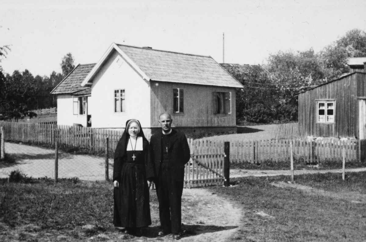 Anno Domkirkeodden, Signe og Leif Larsen utenfor barndomhjemmet "Hammersborg" på Solvang, Sanglundvegen 15, 2319 Hamar. I bakgrunnen sees Sollivegen 8. Ca. 1950-1955. Signe Larsen f. 1914- d. 1983 og Leif Larsen f. 1905-d. 1977. Leif gikk inn i fransiskanerordenen og Signe ble søster i St. Karl Borromeusordenen og tok…