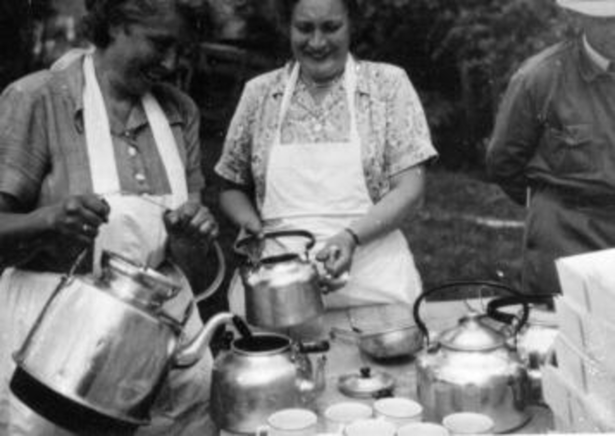 Anno Domkirkeodden, To damer med forklær skjenker kaffe. Kaffekjeller, kopper, øse. Ringsaker Almenning.