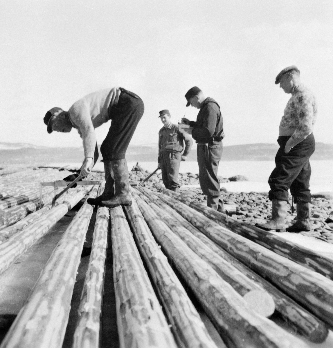 Anno Domkirkeodden, Gruppe menn klaver (måler), stikker (fløyholder) med stikkbok, to påslåere. Tømmermåling på stranda ved Mjøsa på Grefsheim, Nes, Hedmark.s.