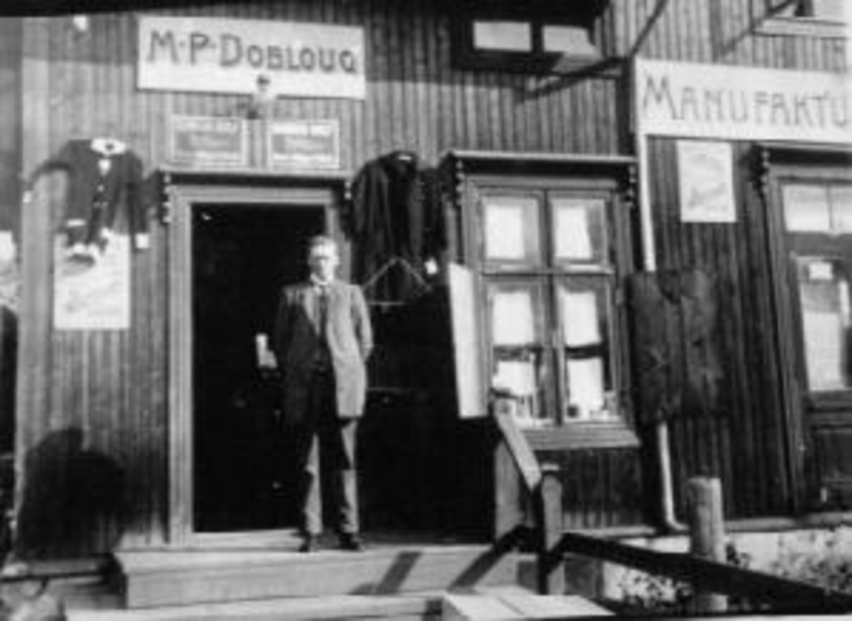 Anno Domkirkeodden, Eksteriør, manufakturforretning, M.P. Dobloug, Moelv. Reklameskilt på veggen. Kjøpmann i døra.
