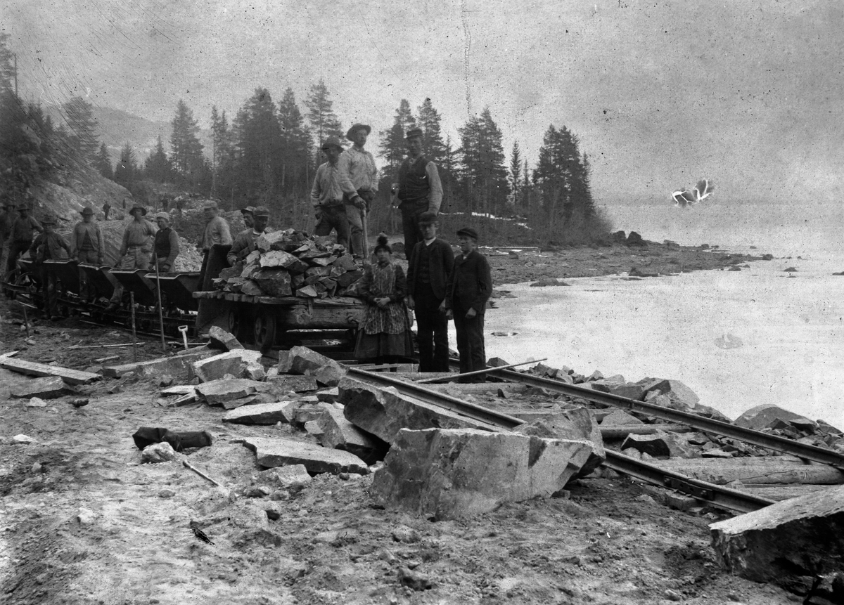 Anno Domkirkeodden, Anleggsarbeid, jernbaneutbygging. Fjellskjæring og steinfylling til jernbane. Arbeidere transporterer stein nedenfor Berg gård på Brøttum, Ringsaker.