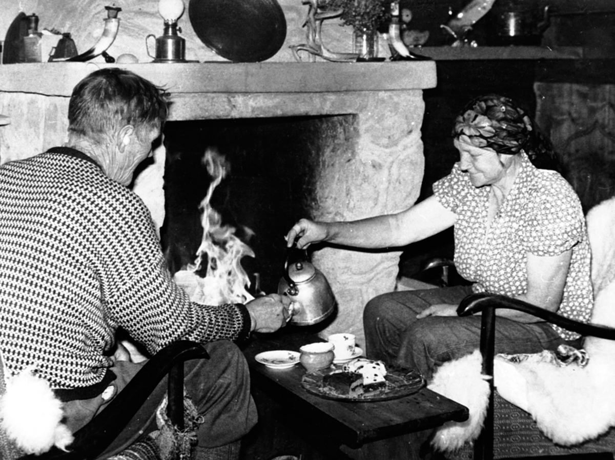Anno Domkirkeodden, Trygve og Julie Solbakken foran peisen på hytta, Gammelskolla, Ringsakerfjellet. Kaffekos.