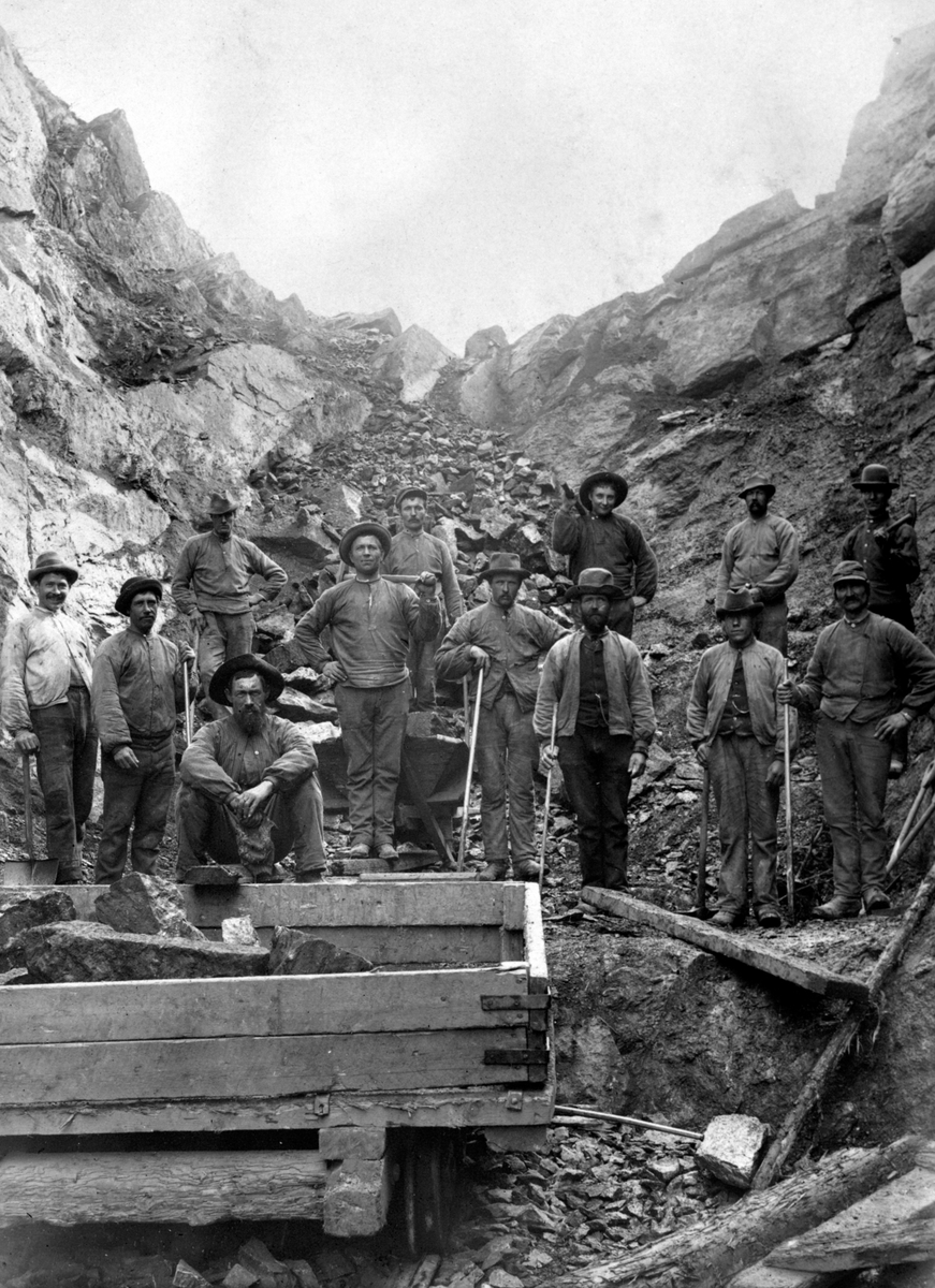 Anno Domkirkeodden, Jernbaneutbygging. 16 jernbanearbeidere ved Domstuetunnelen, Ringsaker. Vogn med stein i forgrunnen.