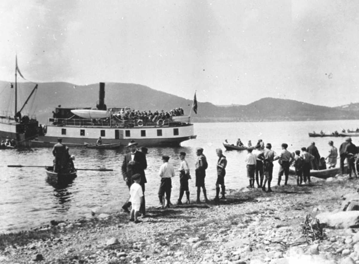 Anno Domkirkeodden, Mjøsbåten D.S Skreia ved Nerkvern stranda i Brumunddal. Brumunddal Sangforening og Orkesterforeningen klar for tur til Hovinsholm på Helgøya. Robåter som frakter folk i forgrunn. Karl Solhaug m/sønnen Magne Solhaug i forgrunnen.