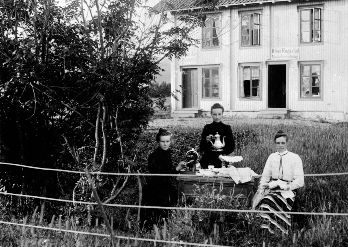 Anno Domkirkeodden, 3 damer drikker kaffe i hagen. Oline Rognstad gift Aas med to sydamer. eksteriør Negård, Olsengården, posthus her 1915-20. I huset bak Arnt Aas skotøyforretning, Oline Rognstads moteforretning, Nygata, Brumunddal.