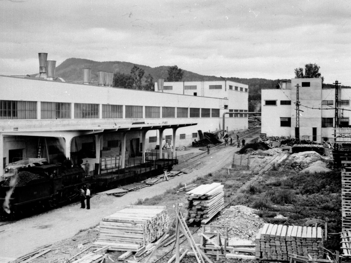 Anno Domkirkeodden, Oversikt Berger Langmoen A/S, fabrikkområdet, Brumunddal, wallboardfabrikken til venstre, damplokomotiv ved lasterampa, menn som arbeider.