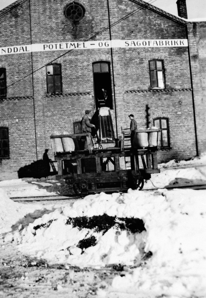 Anno Domkirkeodden, Frakt av potetmelsekker ved A/S Brumunddal Potetmel og Sagofabrikk. Vinter. Tre menn lesser spesiell jernbanevogn.