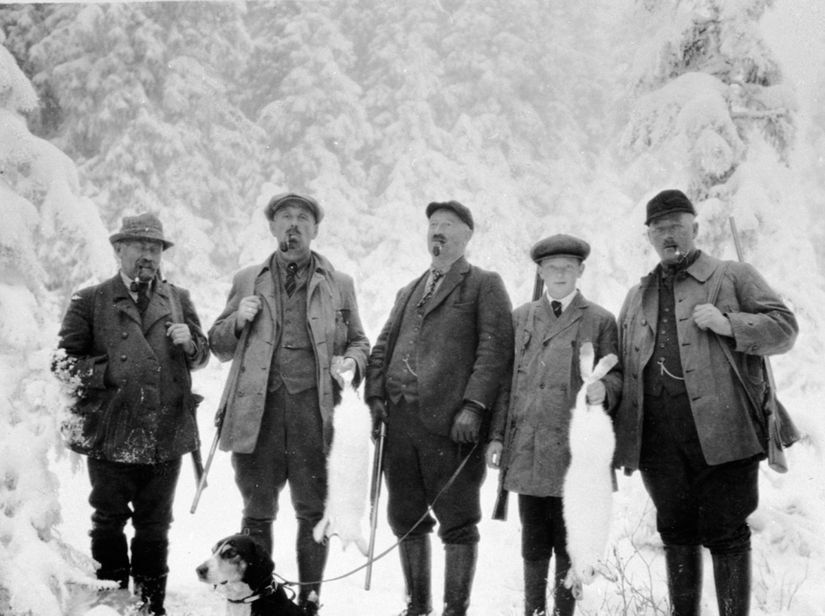 Anno Domkirkeodden, Gruppe jegere med gevær og hund, harejakt. Fra venstre er Einar Narud, Ole Sølvsberg, Anders Opsal, Jørgen Opsal, Lars Opsal, Kompåsen, Veldre, Ringsaker.
