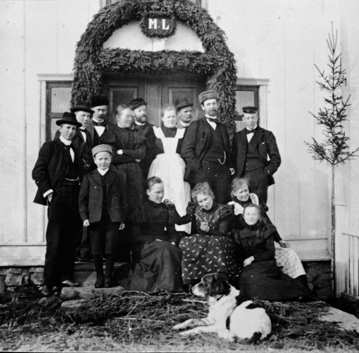 Anno Domkirkeodden, Bergravelse etter Marte Løken, Løken østre, Veldre, Ringsaker. Bardekorasjon over ytterdør med initialer M.L. Foran fra venstre er Hans Ulven, Lally Skappel, Lulla Hersoug, Albert Sigstad, ukjent. Nummer 4 bak er mor til Hans og Per Ulven, nummer 6 er Mimmi Løken, 7 er Jacob Ruud, 9 er Per Ulven.