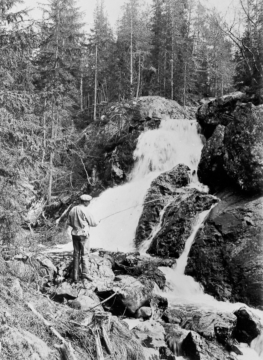 Anno Domkirkeodden, Liten foss i Faldbekken som renner ut i Moelva ved Næroset, Ringsaker. Mann fisker med stang.