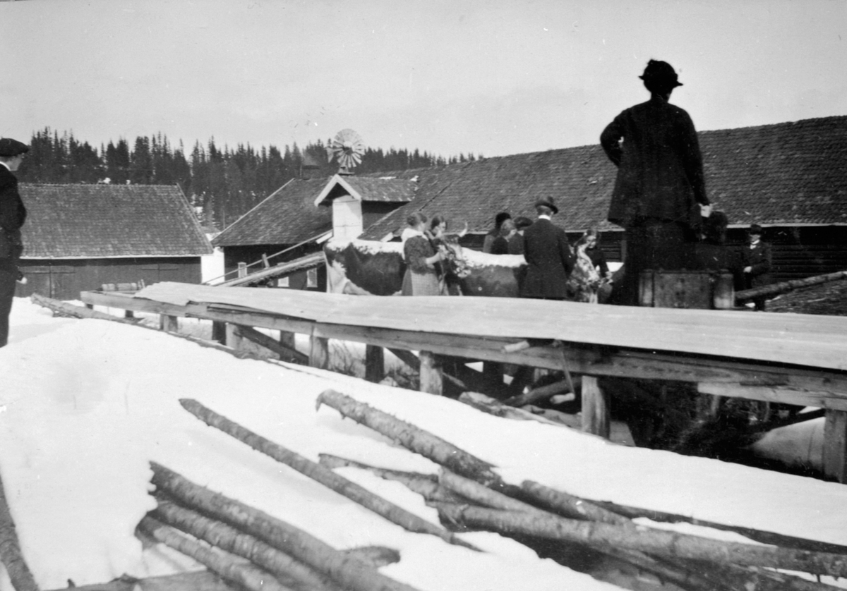 Anno Domkirkeodden, Sagbenken på Eik, Helgøya. Telemarksku på tunet, Gamle låven og fjøset i bakgrunnen. Vindmølle på taket av låven. Vinter. Gruppe mennesker.