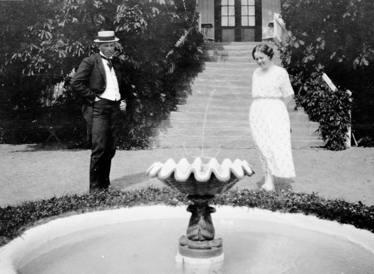 Anno Domkirkeodden, Dame og mann ved fontene ved inngangspartiet fra hagen på Hovelsrud, Helgøya.