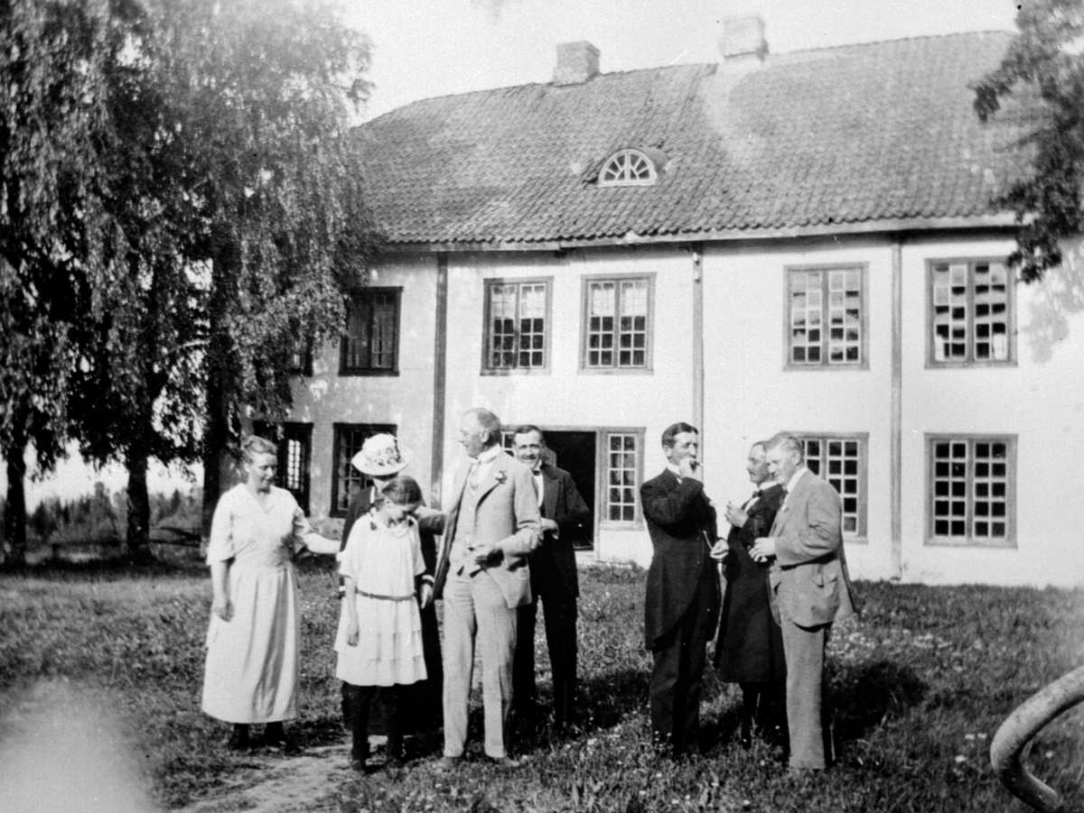 Anno Domkirkeodden, 8 personer foran den gamle hovedbygningen på Eskerud, Helgøya. Fra venstre Helene Vien, datter til Major Damm, Kristine Damm, Nils Damm, Ola Brevig, Thorbjørn Brevig, Torolf Vien og Sigurd Brevig. Hanna Lovise Brevig sin barnedåp i 1921.