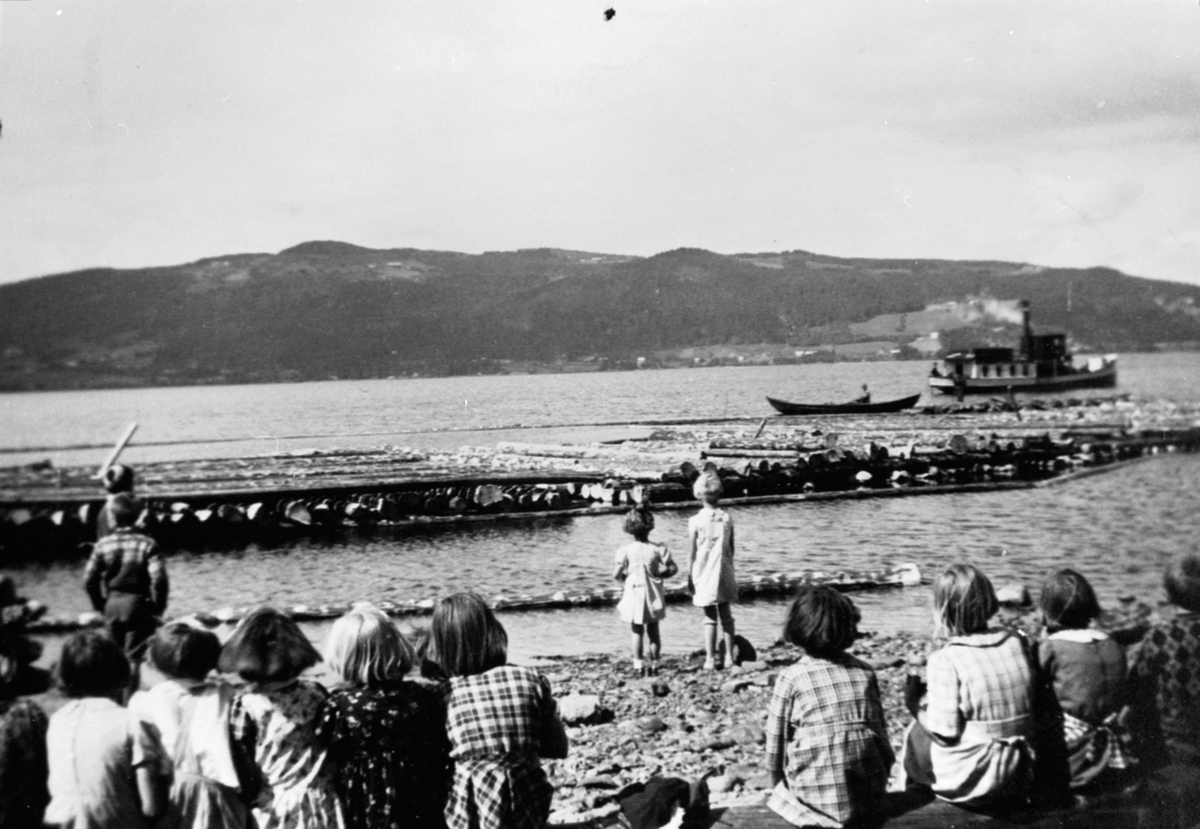 Anno Domkirkeodden, Tømmertransport/fløting på Mjøsa med båt: Barn som tilskuere i strandkanten.