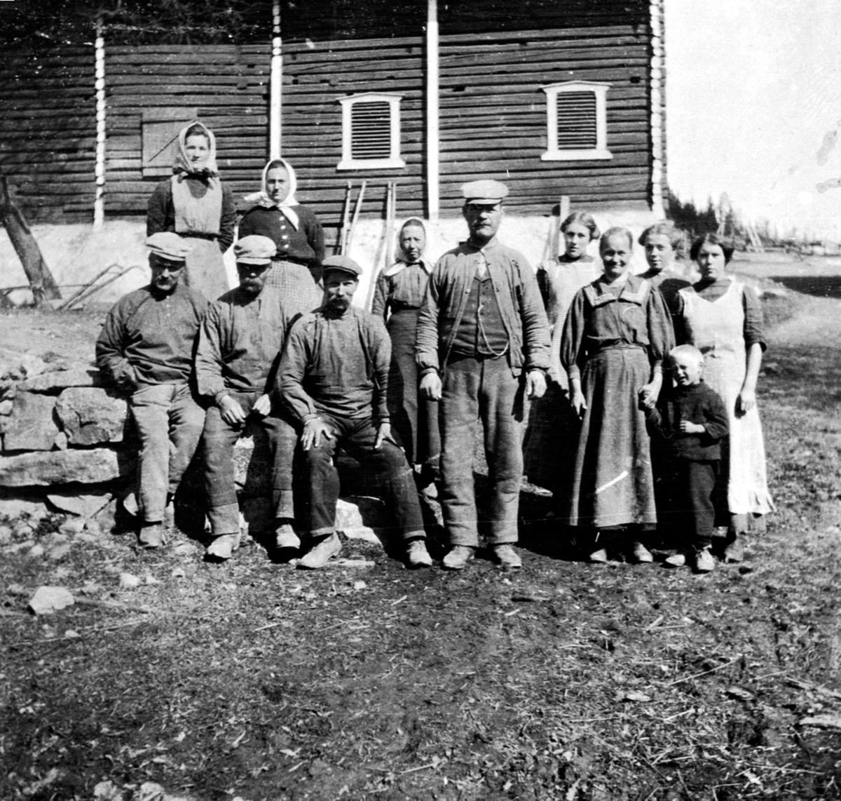 Anno Domkirkeodden, 12 arbeidere foran gamlelåven på Hovelsrud, Helgøya. Bak fra venstre er Albertine Engeland (1884-1955), Susanne Bakken (1885-1958). Foran fra venstre er Olaf Bakken (1882-1975), Adolf Engeland (1884-1967), Peder Skogheim (1876-1957), Kristine Kval f.1856, Olivius Maurud f.1869, Borghild Gustavsen f…