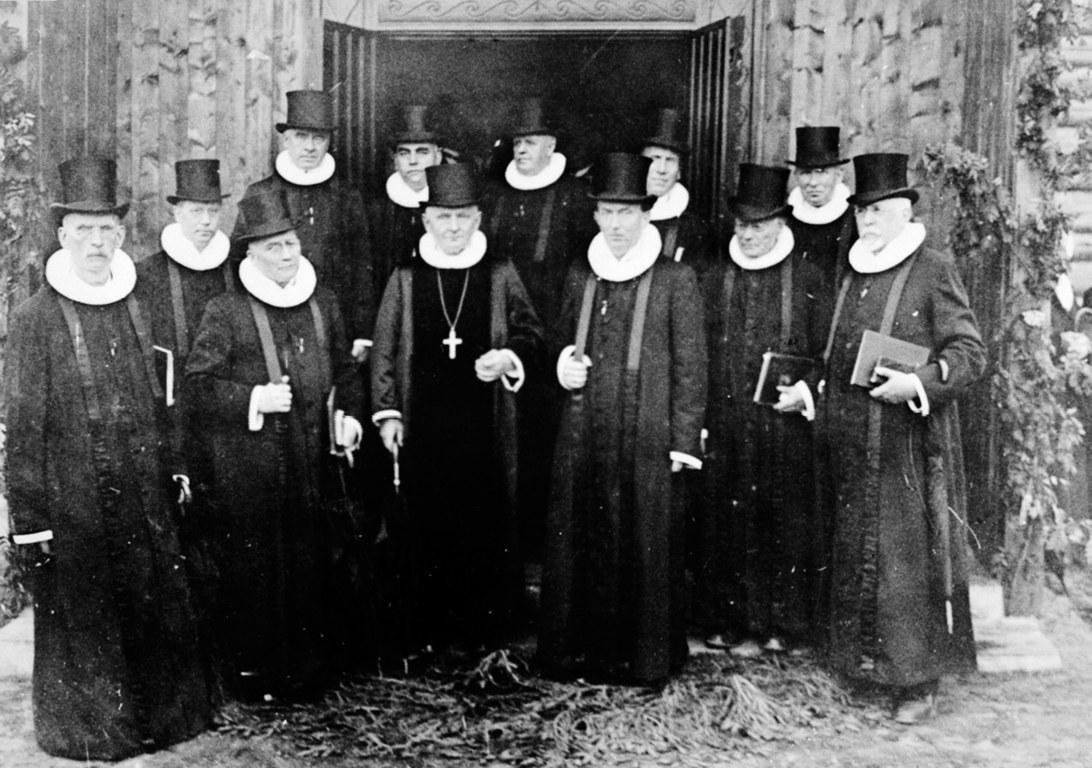 Anno Domkirkeodden, Innvielse av Mesnalien kapell den 13. september 1933. Gruppe med prester foran inngangen. Fra venstre er Paulsen (Løten), Hexeberg (Veldre), Lund (Nes), Eger (Hamar), Winsnes (Stange), biskop Bjønnes Jacobsen, Kjær (Stange), Hauge (Brøttum), Svendsen (Veldre, Kaldor, Romedal), Brage Høyen (Lilleham…