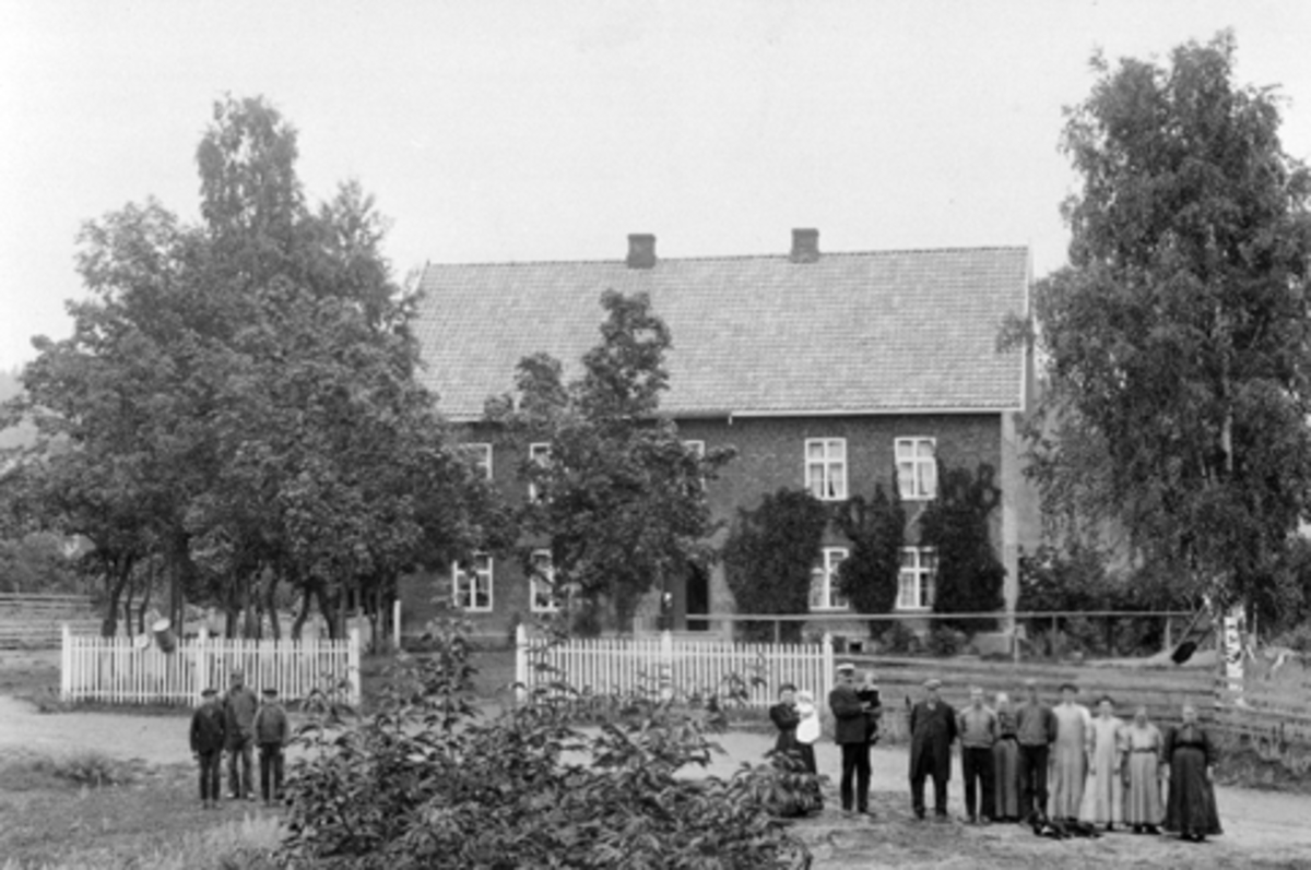 Anno Domkirkeodden, Eksteriør gardsbruket Mellom-Kise, Nes, Hedmark. Sjølfolk og arbeidsfolk på tunet. Anna Dorthea Haugen (1883-1965) med Anna Marie (1910-1992) på armen, Christian Evensen Haugen (1847-1914) med Even Arnt (1909-1962). Resten er ukjente.