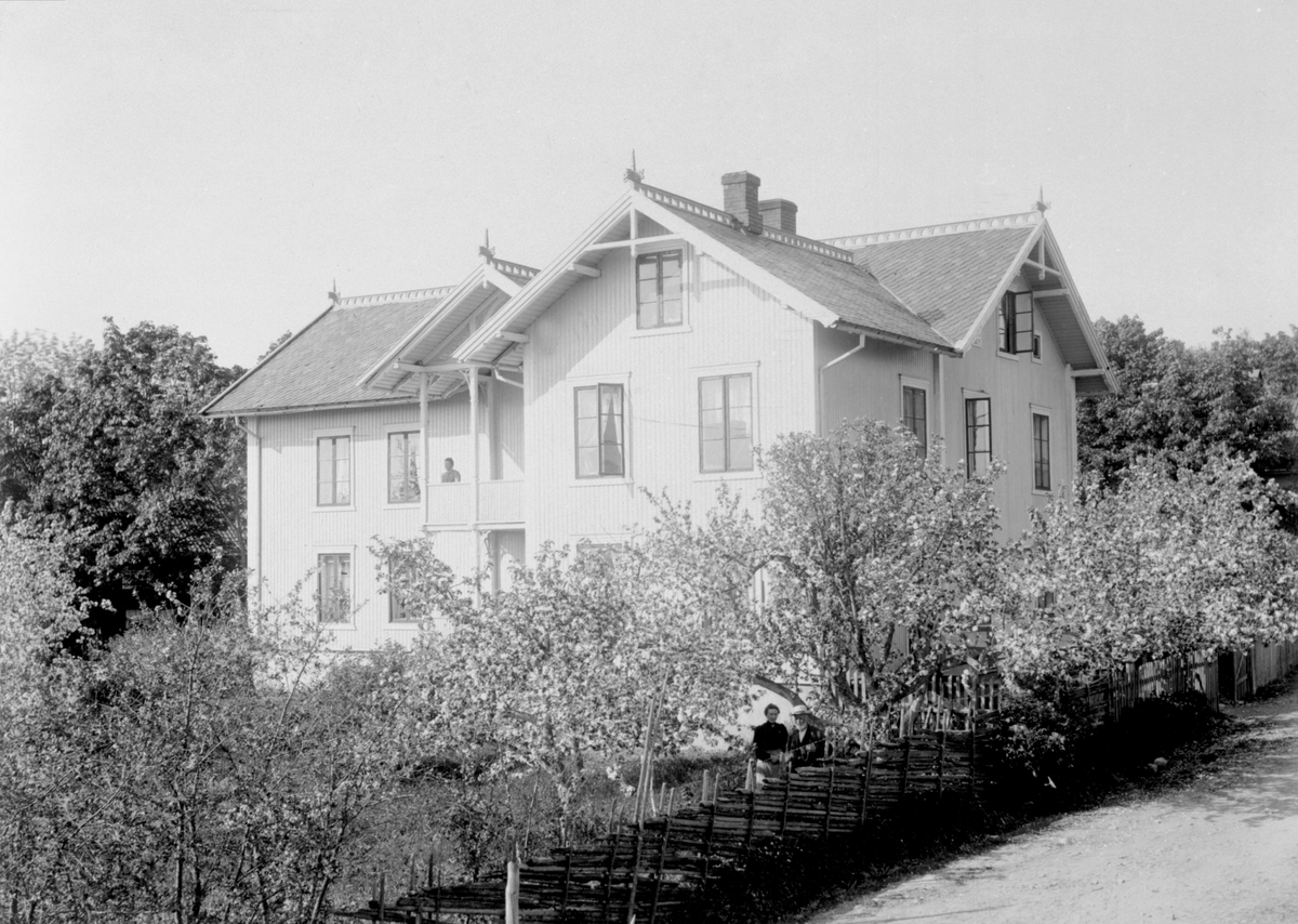 Anno Domkirkeodden, Eksteriør hovedbygningen på Helgeby, Nes, Hedmark. Syverine Helgeby (1866-1923) på veranda. Anna Lie (1869-1934) og Jacob Lie (1832-1918) i hagen ved skigard.