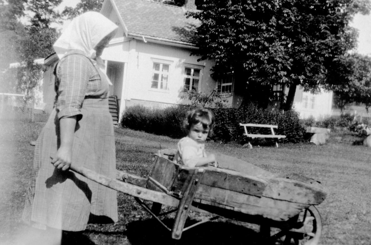 Anno Domkirkeodden, Budeie Sina Nordby fra Øyer, f.1884 med trillebår. Peder Barfoed, barnebarnet til Ole Martin Helgeby (1857-1933) i trillebåra. Helgeby, Nes, Hedmark.