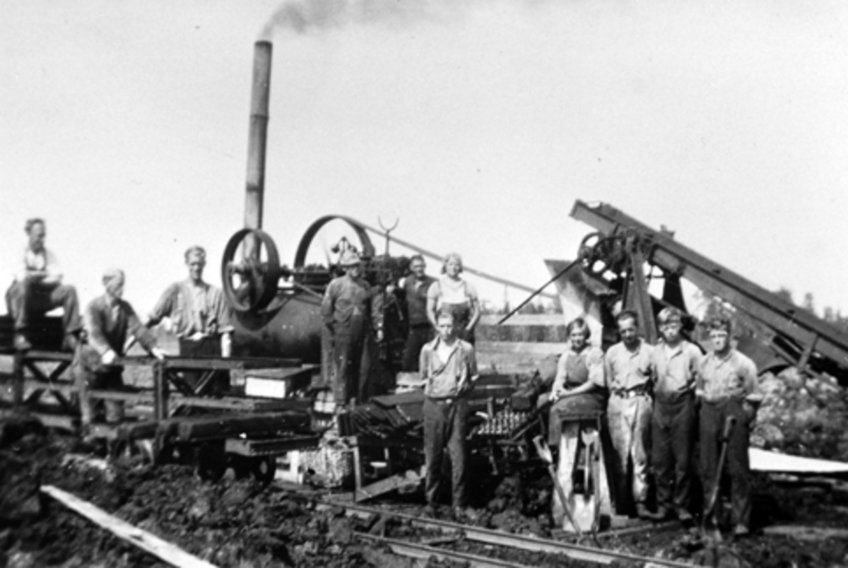 Anno Domkirkeodden, Høljamyra torvfabrikk, Furnes Almenning. Torvdrift i Høljamyra startet i 1934. Gruppe arbeidere foran lokomobil og elevator.