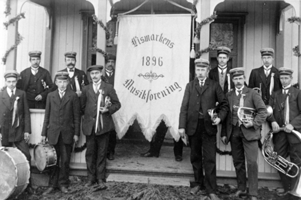 Anno Domkirkeodden, Musikere fra Lismarken Musikkforening med instrumenter og fane utenfor den gamle skolen i Lismarka, Ringsaker. Fra venstre er Børre Bjørnsrud, Torstein Midtlien, Ole Lillehagen, Nils Midtlien, Johannes Olasveen, Nils Bjørnsrud. Andre rekke fra venstre er Halvor Midtlien, Lars Martinsen, Nils Øverli…
