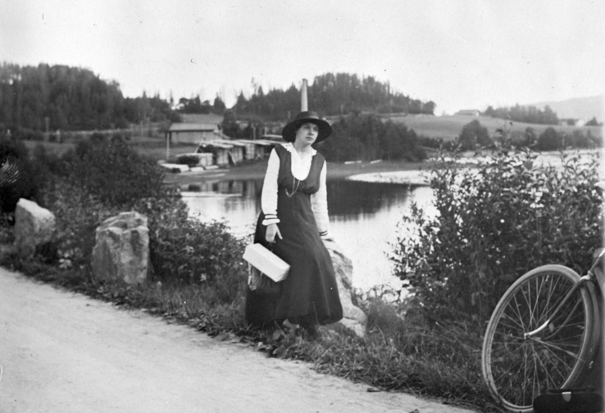 Mikkel Sveinhaug, Frk. Brødrup på sykkeltur ved Korgerstuvika. I bakgrunnen Steinvik sagbruk som tilhørte Julius Olsen. 1924.